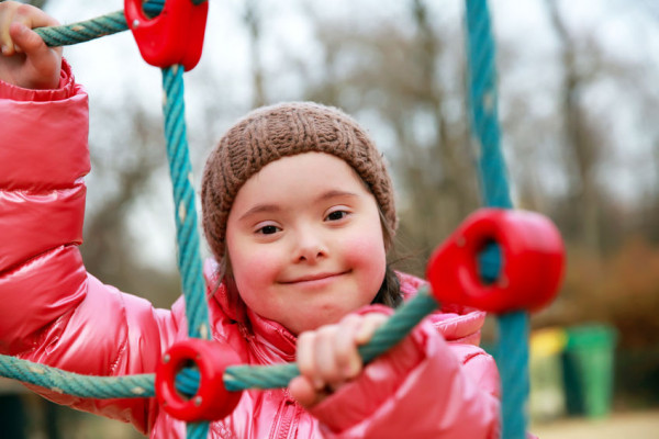 A young girl with Down Syndrome smiles as she climbs a structure in a playground
